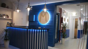 A reception desk with a blue and white color scheme, a round mirror above it, and a potted plant to the left. - Hostal Miranda (Blanes)
