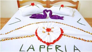 A bed with a white bedspread, purple pillows, and a decorative arrangement of flowers and beads spelling "LAPERIA".