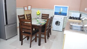 A compact kitchen with a refrigerator, washing machine, and a dining table with chairs.