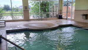 An indoor swimming pool with clear glass walls, a tiled floor, and a bench outside. - Springhill Suites Houston Westchase (Houston)