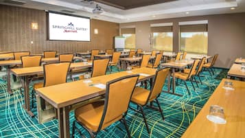A conference room with tables and chairs, a projector screen, and a carpeted floor.
