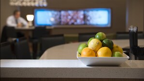 A bowl of fruit on a counter with a blurred background of a person and a television screen. - Springhill Suites Houston Westchase (Houston)
