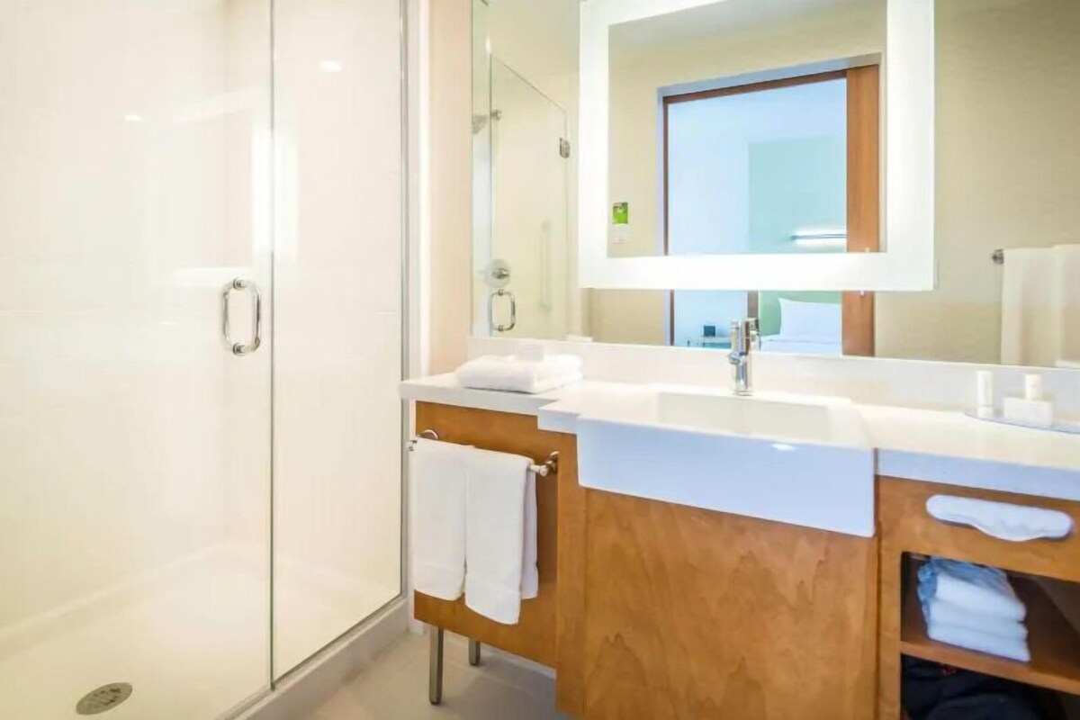 A modern bathroom with a glass shower enclosure, a wooden vanity with a white countertop, and a large mirror above the sink.
