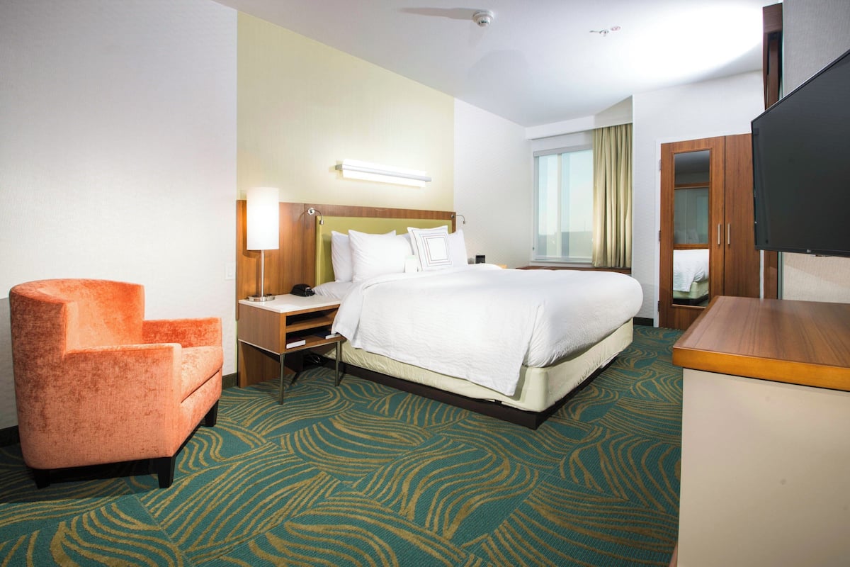 A hotel room with a bed, a chair, a desk, a television, and a window with curtains.