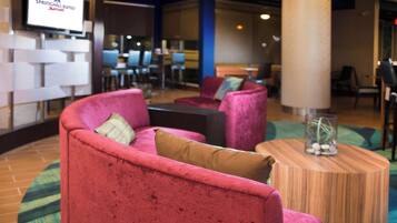 A hotel lobby with red sofas, a wooden coffee table, and a television displaying the SpringHill Suites Marriott logo.