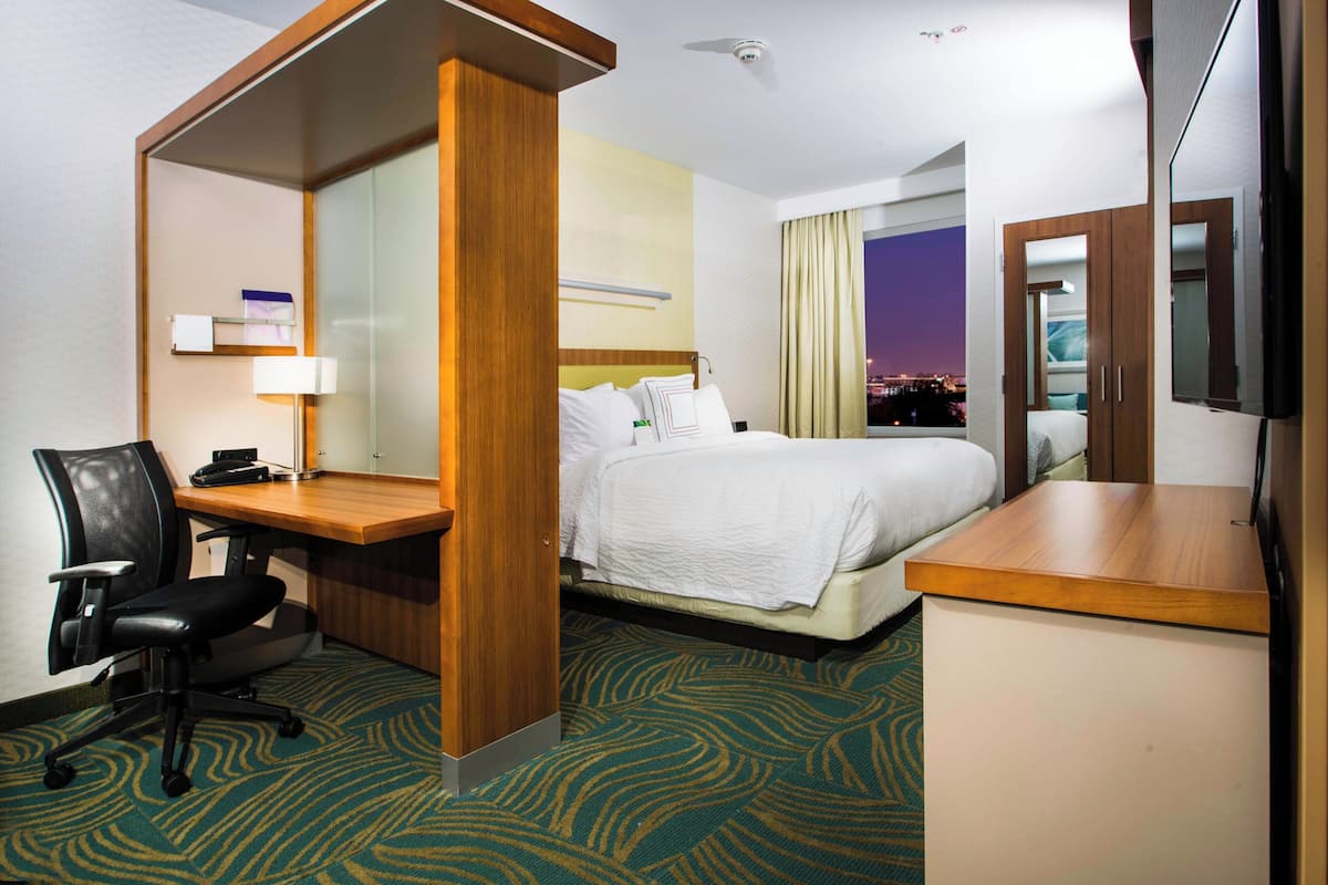 A hotel room with a bed, desk, chair, and a TV.