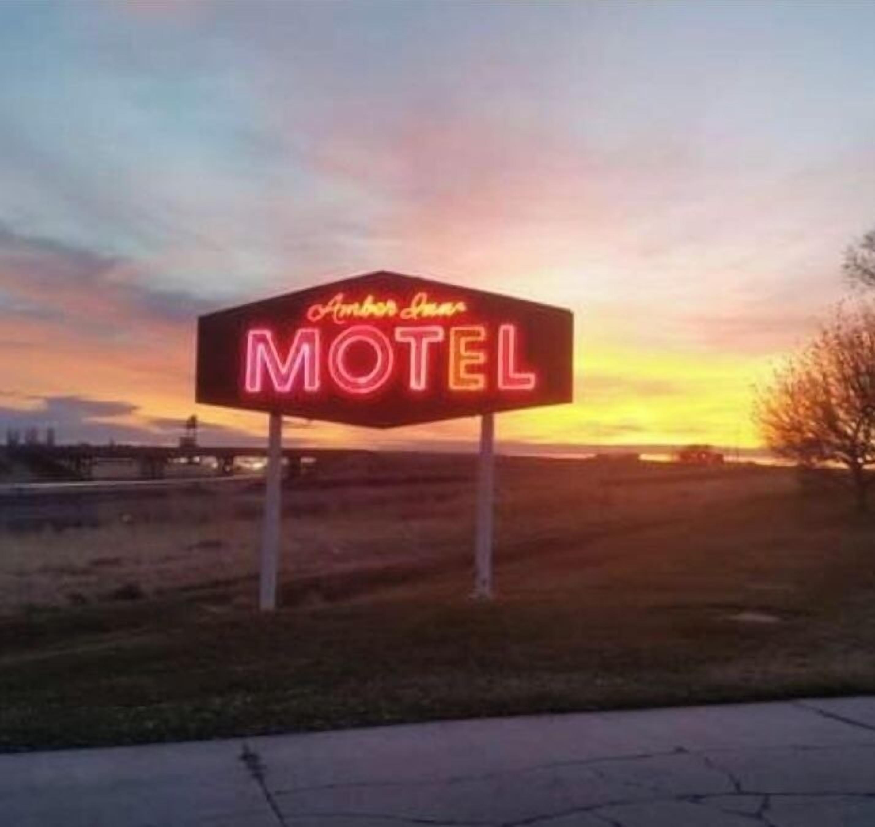 Un letrero de motel neón con el nombre 'Amber Inn' contra un cielo al atardecer.