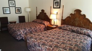 Quarto de hotel com duas camas, uma mesinha de cabeceira, um abajur e quadros nas paredes.