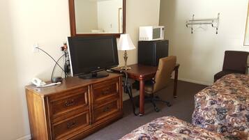 A hotel room with a wooden dresser, a desk with a television, a microwave, a chair, and a bed with patterned bedding.