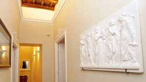A hallway with a tiled floor, a white wall with a relief sculpture, and a wooden ceiling. - Madonna de’ Monti Suites  (Rome)