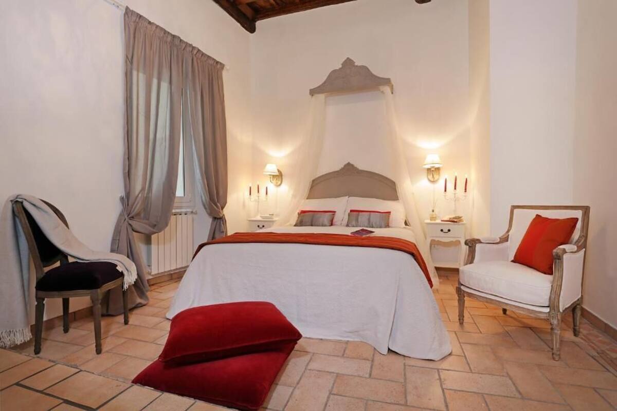 A bedroom with a bed, two bedside tables, a chair, a window with curtains, and a red pillow on the floor.