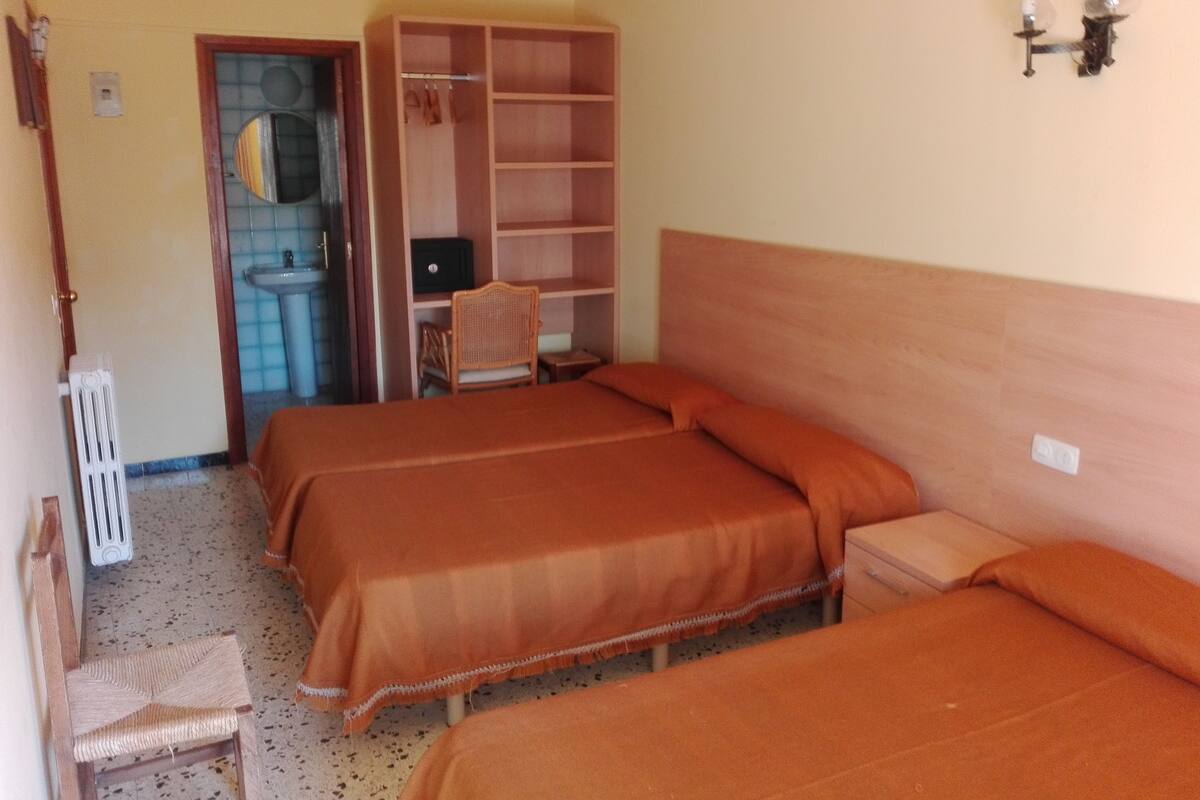 A bedroom with two beds, a wooden wardrobe, a chair, and a small table.