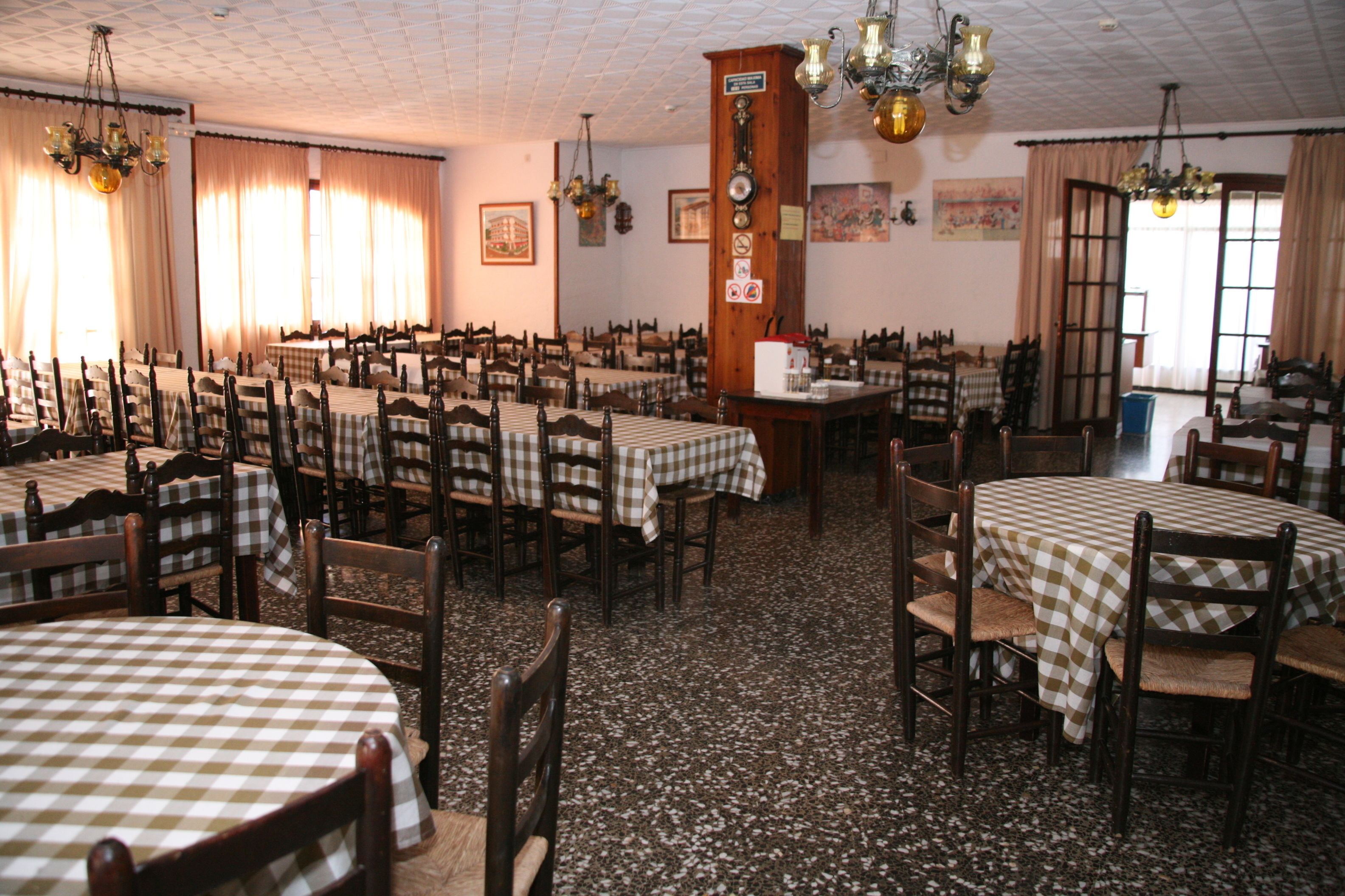 Une grande salle à manger avec de nombreuses tables et chaises, des murs en bois et un sol carrelé.