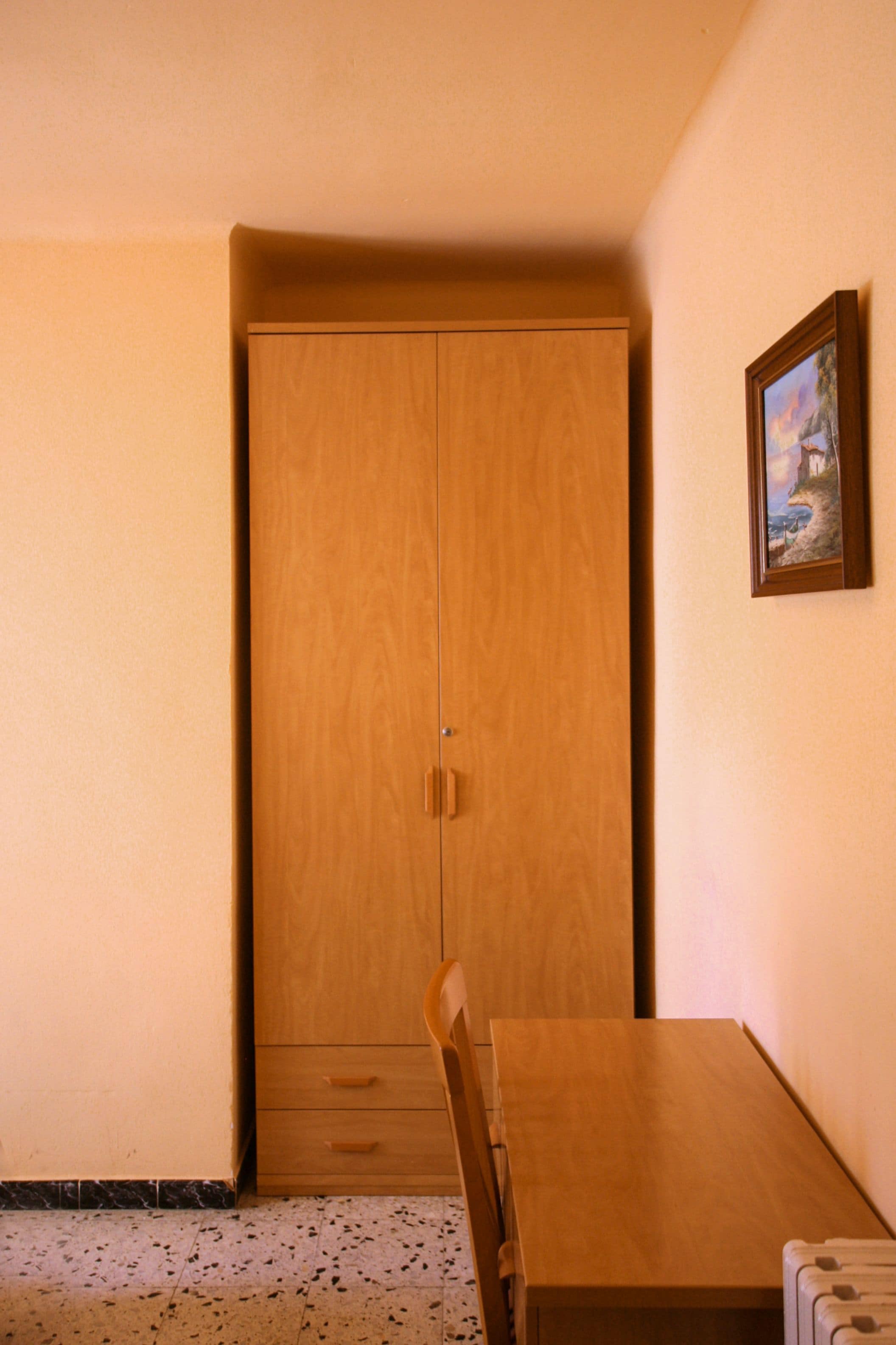 Una habitación con un armario de madera, una mesita y un cuadro en la pared.