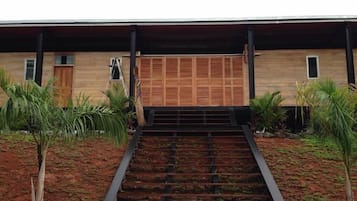 Un edificio moderno con fachada de madera, una escalera de metal que lleva a una puerta y plantas tropicales alrededor.