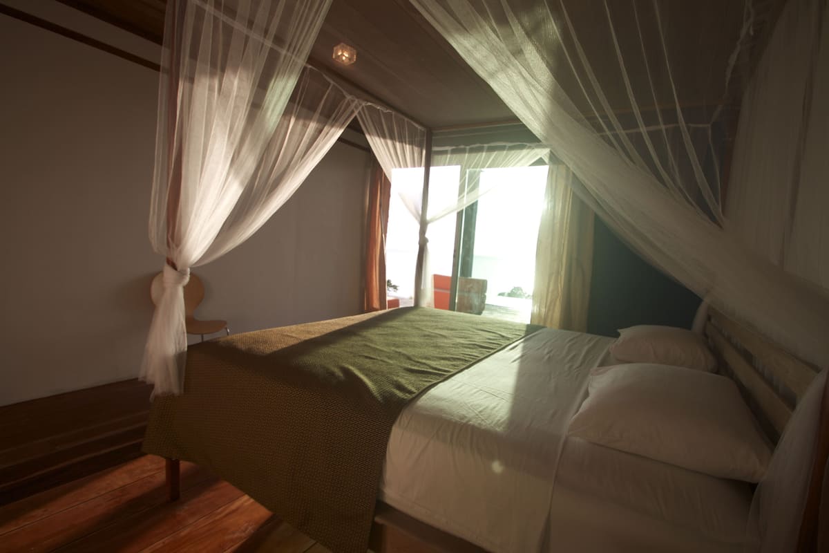 Quarto com cama, um banco de madeira e janela com cortinas.