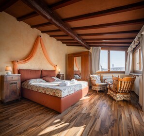 A bedroom with a large bed, wooden floor, and a window with a view. - Novella House (Florence)