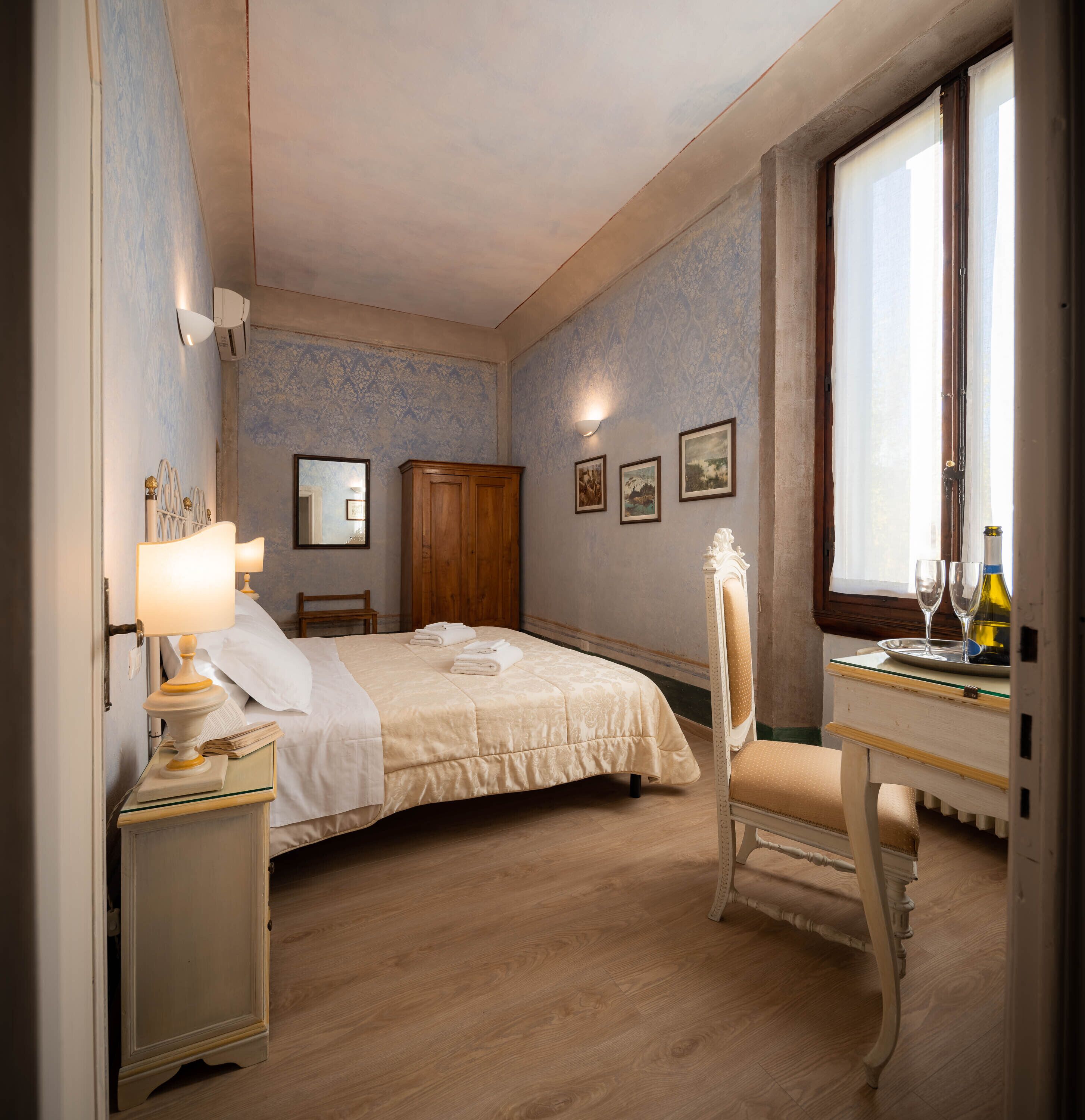 A bedroom with a bed, a nightstand, a chair, a wooden wardrobe, and a window with curtains.