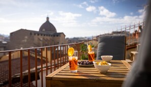 A wooden table with drinks and snacks on a balcony overlooking a cityscape with a prominent dome building. - Novella House (Florence)