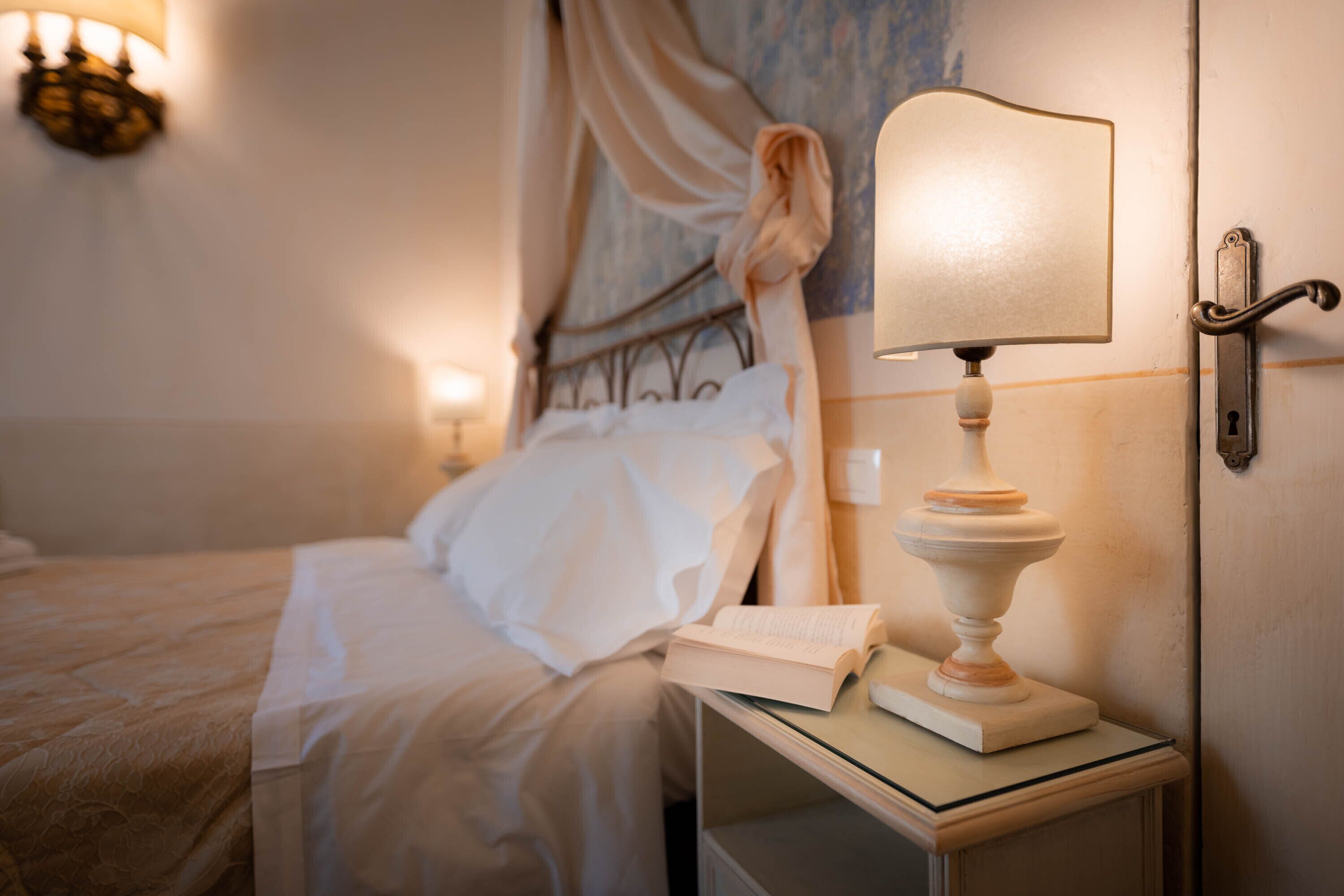Ein ordentlich bezogenes Bett mit weißen Leinen, eine Nachttischlampe und ein Buch auf dem Nachttisch.