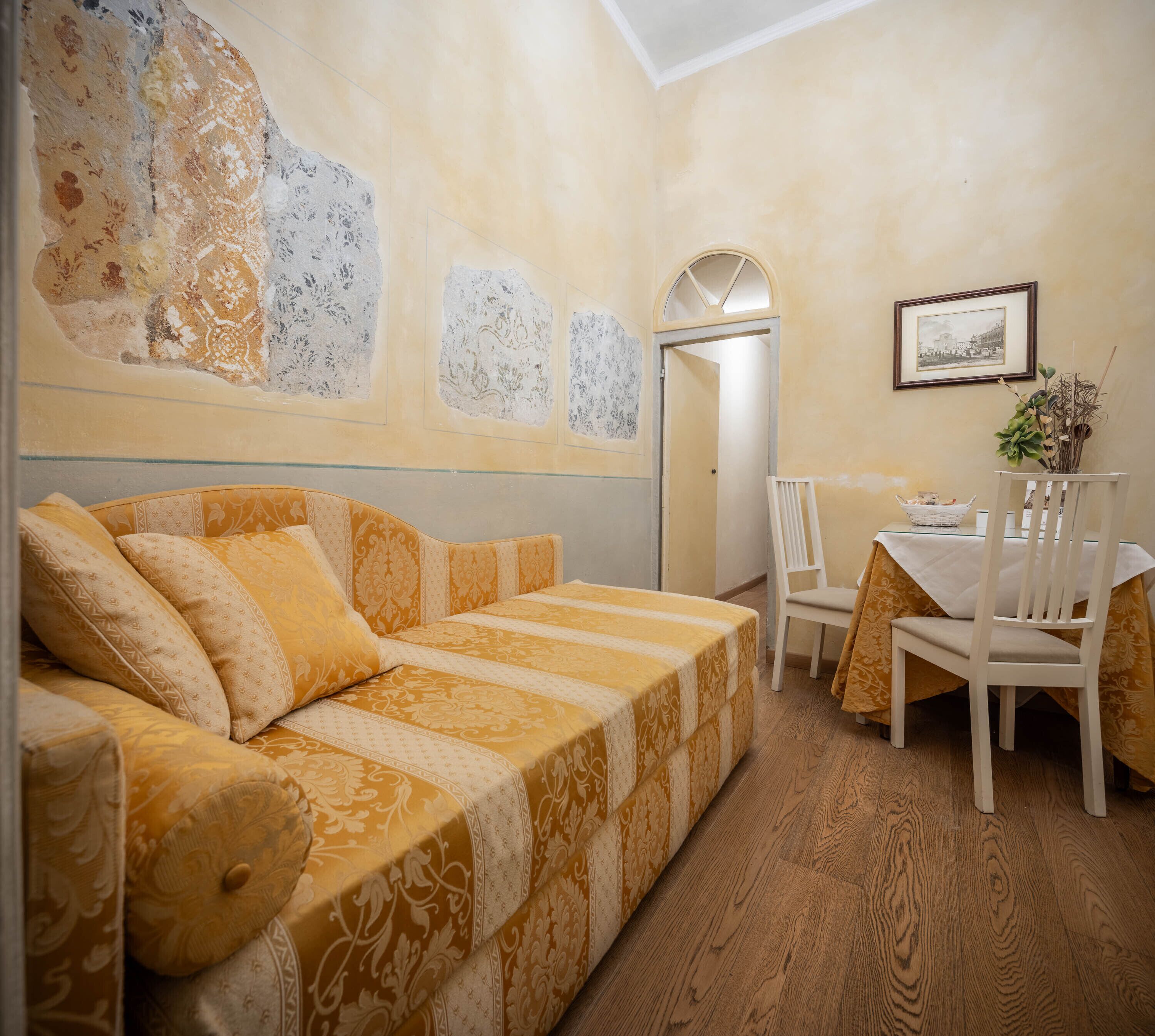 Ein gemütliches Zimmer mit einer gemusterten Couch, einem Esstisch mit Stühlen und einem gerahmten Bild an der Wand.