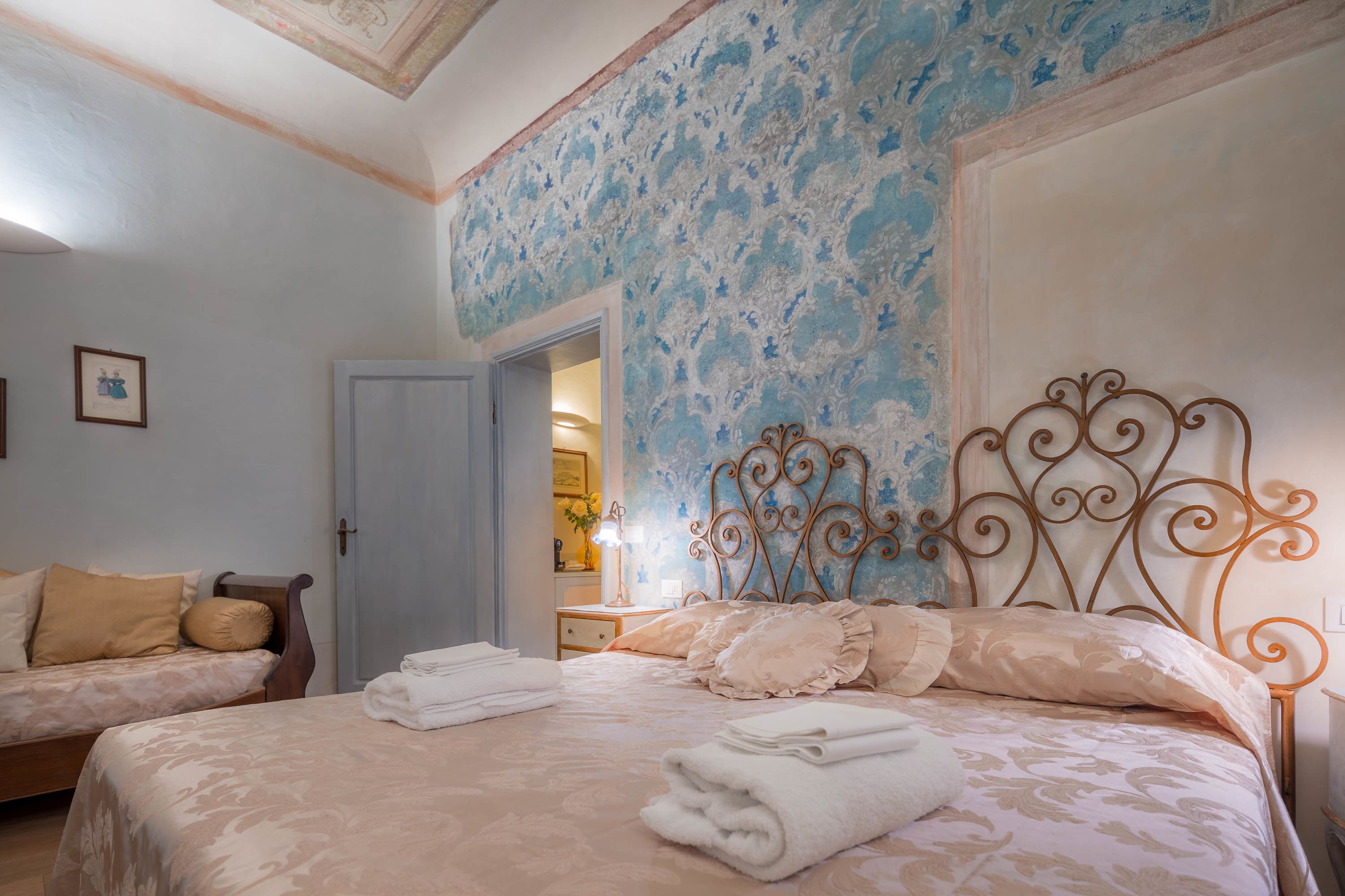 Una camera da letto con due letti, un soffitto decorato e una porta che dà su un'altra stanza.