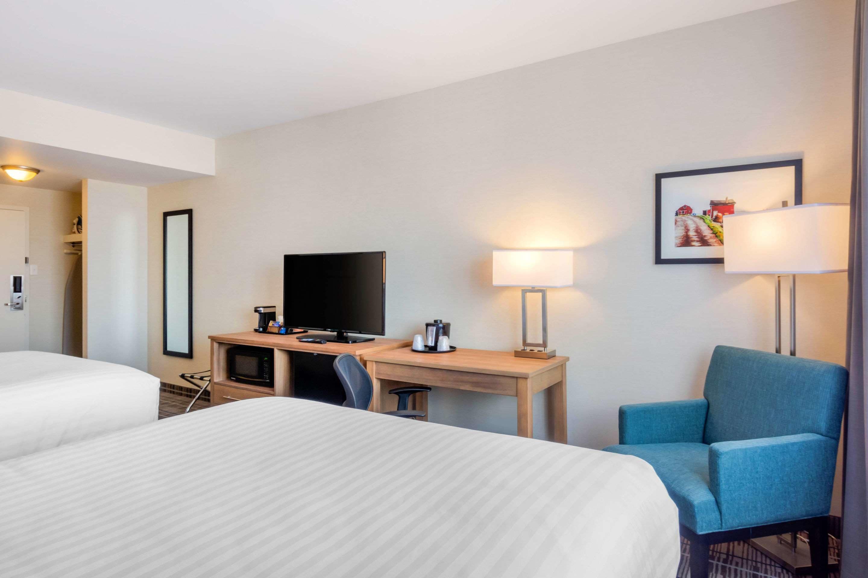 Ein Hotelzimmer mit zwei Betten, einem Schreibtisch, einem Flachbildfernseher, einer Kaffeemaschine und zwei Lampen.