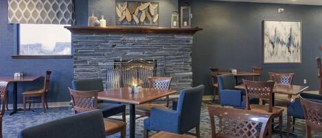 A restaurant with a stone fireplace, blue chairs, and tables.