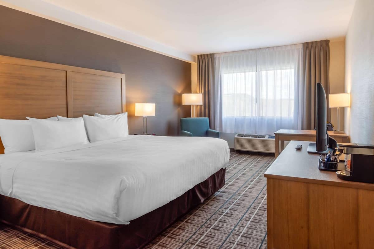 Una habitación de hotel con una cama grande, dos lámparas de noche, un escritorio con televisor y un aire acondicionado.