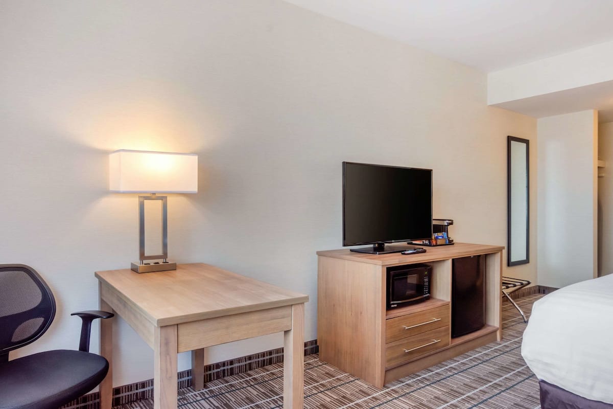 Una habitación de hotel con un escritorio de madera, televisor, microondas y una silla.