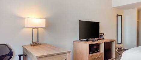 Une chambre d’hôtel équipée d’un bureau en bois, d’une télévision, d’un four à micro-ondes et d’une chaise.