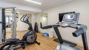 A gym with cardio machines, a treadmill, and a mirrored wall.