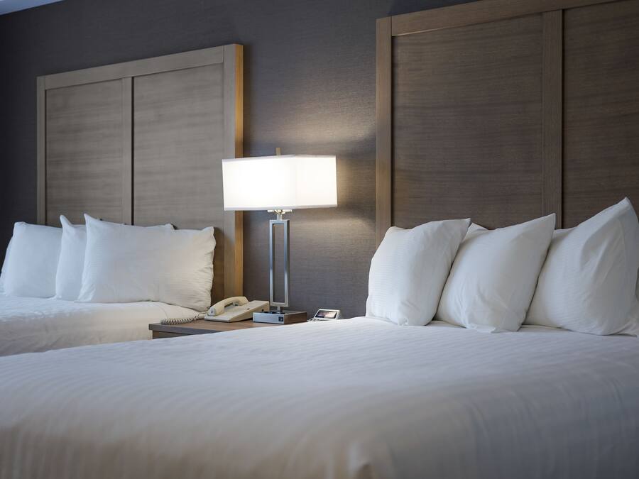 A hotel room with two beds, a nightstand with a lamp, and a phone.