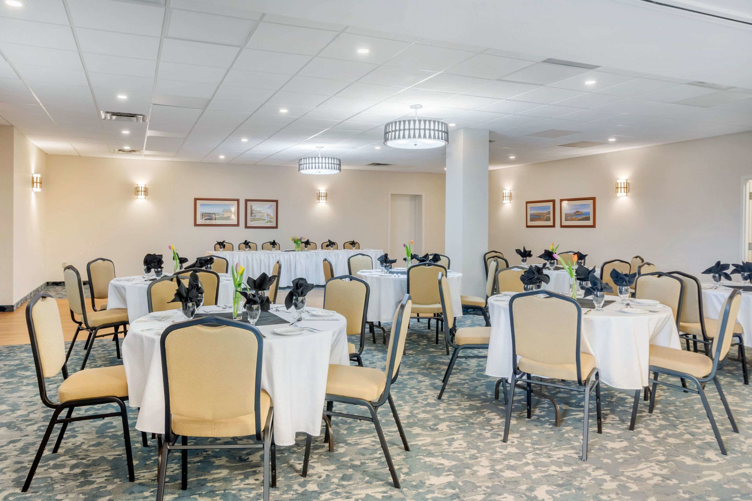 A conference room with round tables, beige chairs, and white tablecloths.