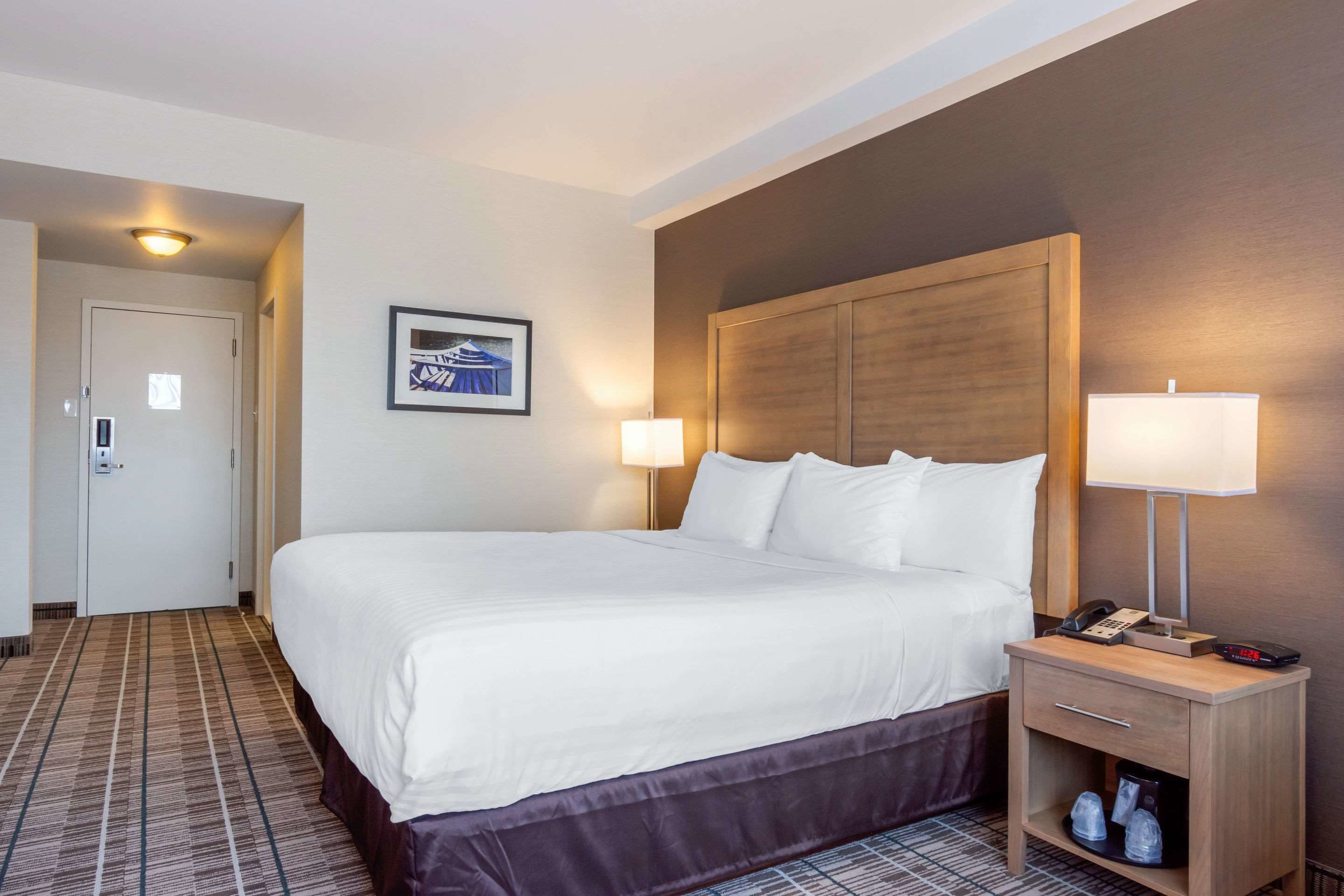 A hotel room with a large bed, bedside lamps, a nightstand with a phone, and a framed picture on the wall.