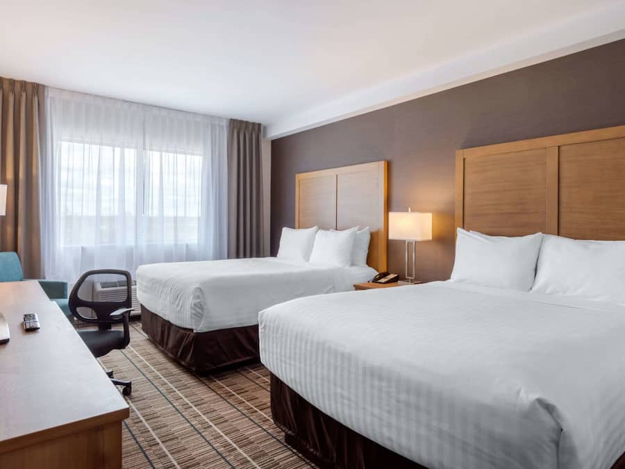 A hotel room with two beds, a desk, a chair, and a TV.