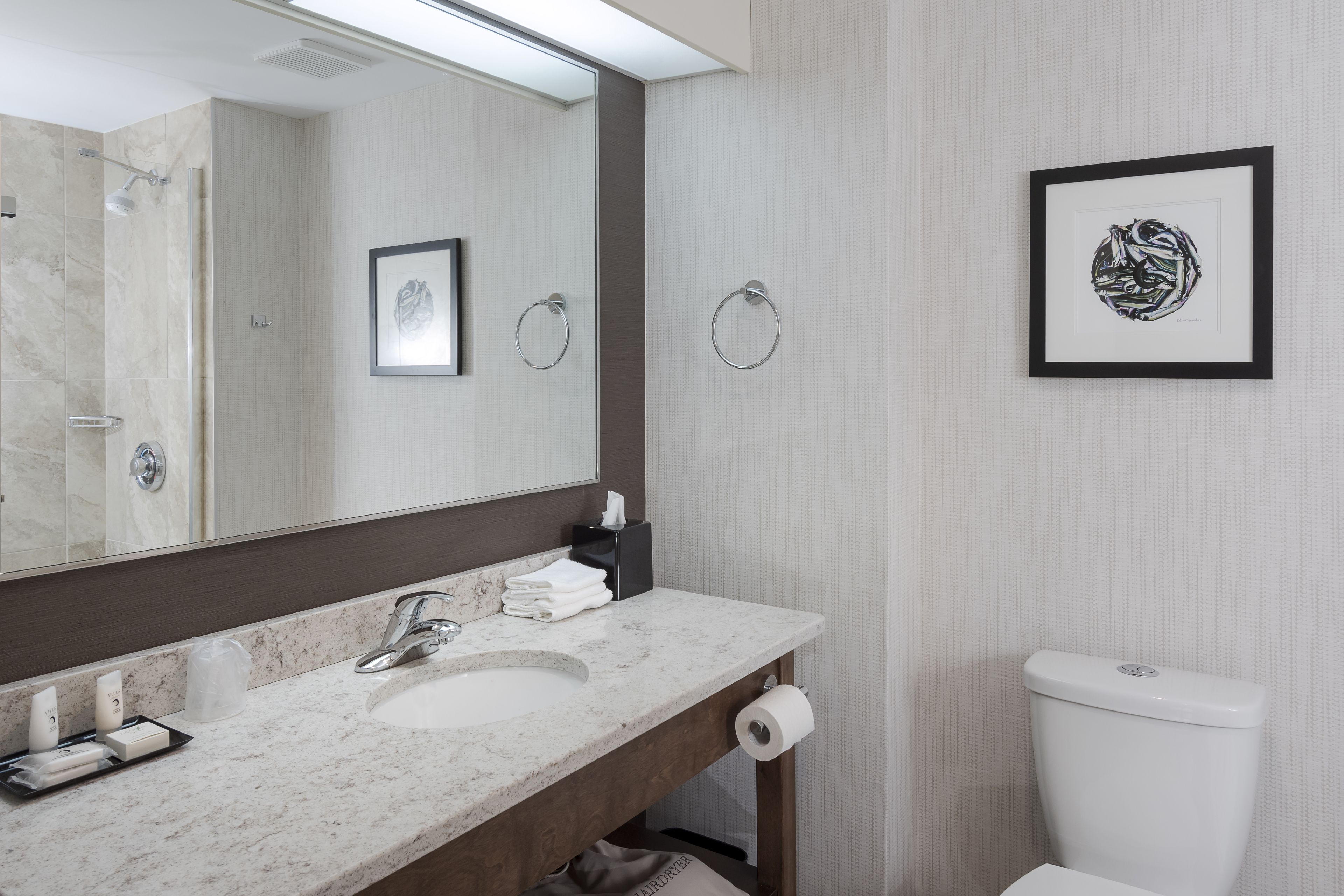 A modern bathroom with a marble sink, a large mirror, a framed artwork, and a toilet.