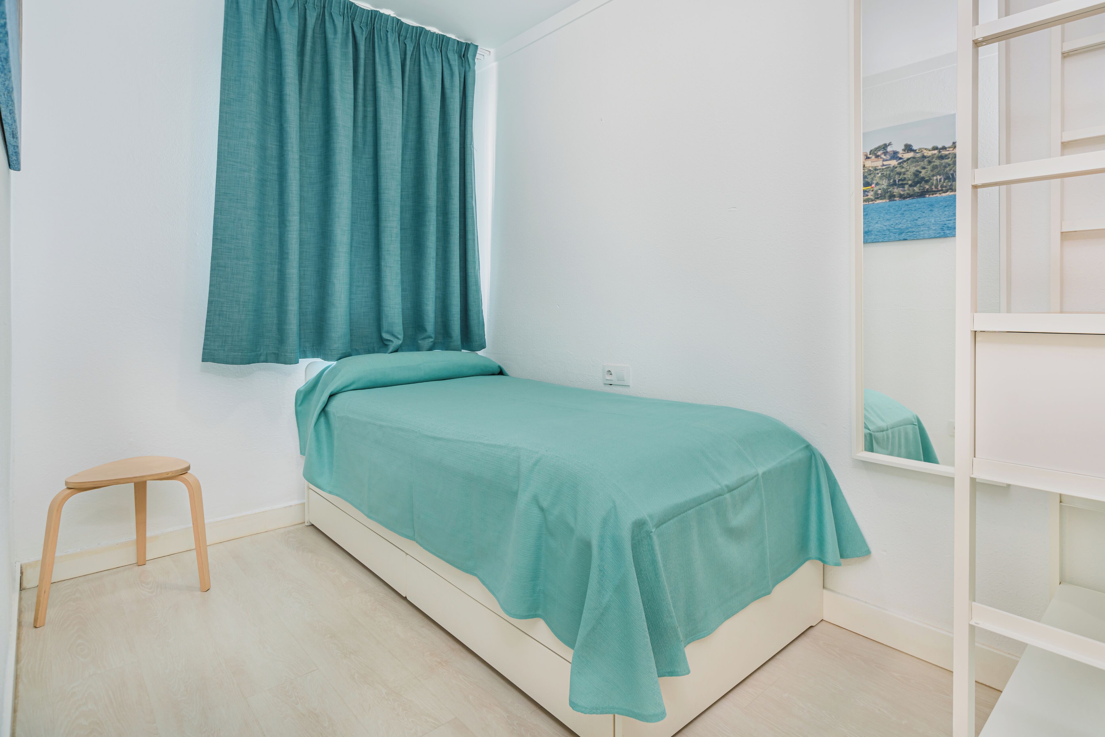 Un lit simple avec une couvre-lit de couleur turquoise dans une pièce aux murs blancs et au plancher en bois.