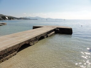 A pier extending into calm waters with clear visibility to distant mountains. - Apartamentos Habitat (Pollenca)