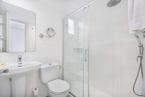 A modern bathroom with a glass-enclosed shower, a toilet, and a sink with a mirror above it. - Apartamentos Habitat (Pollenca)