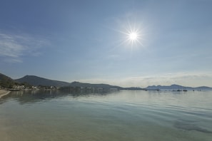 A calm lake with clear water, boats, and mountains in the background. - Apartamentos Habitat (Pollenca)