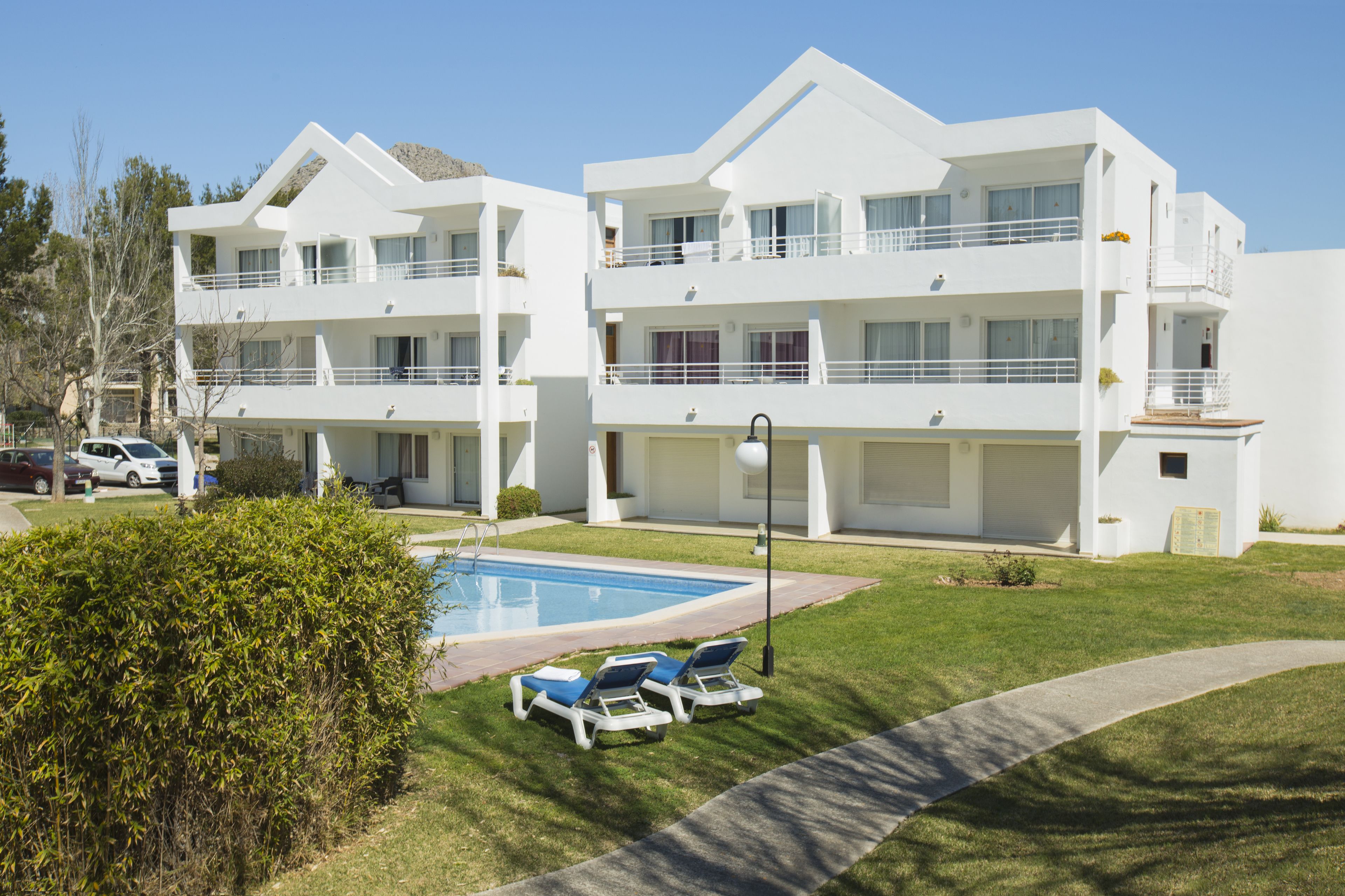 A modern multi-story hotel with a swimming pool, outdoor seating, and a well-maintained lawn.