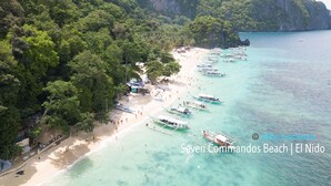 A beach with boats, a sandy shore, and a forested hill. - Swiftlets Inn (El Nido)