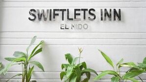 A sign for Swiftlets Inn with a white background and green plants in front. - Swiftlets Inn (El Nido)