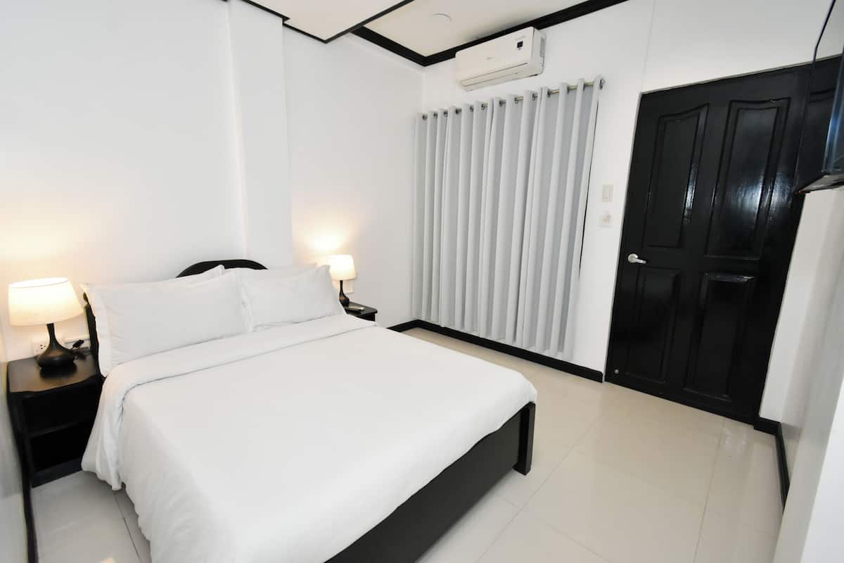 Quarto bem arrumado com cama, mesas de cabeceira, abajur, janela com cortinas e porta.