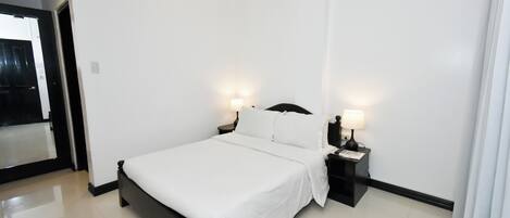 Una moderna camera d'albergo con un letto grande, lampade ai comodini e una porta che conduce a un'altra stanza.