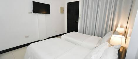 A hotel room with two beds, a flat-screen TV, a door, and a curtain.
