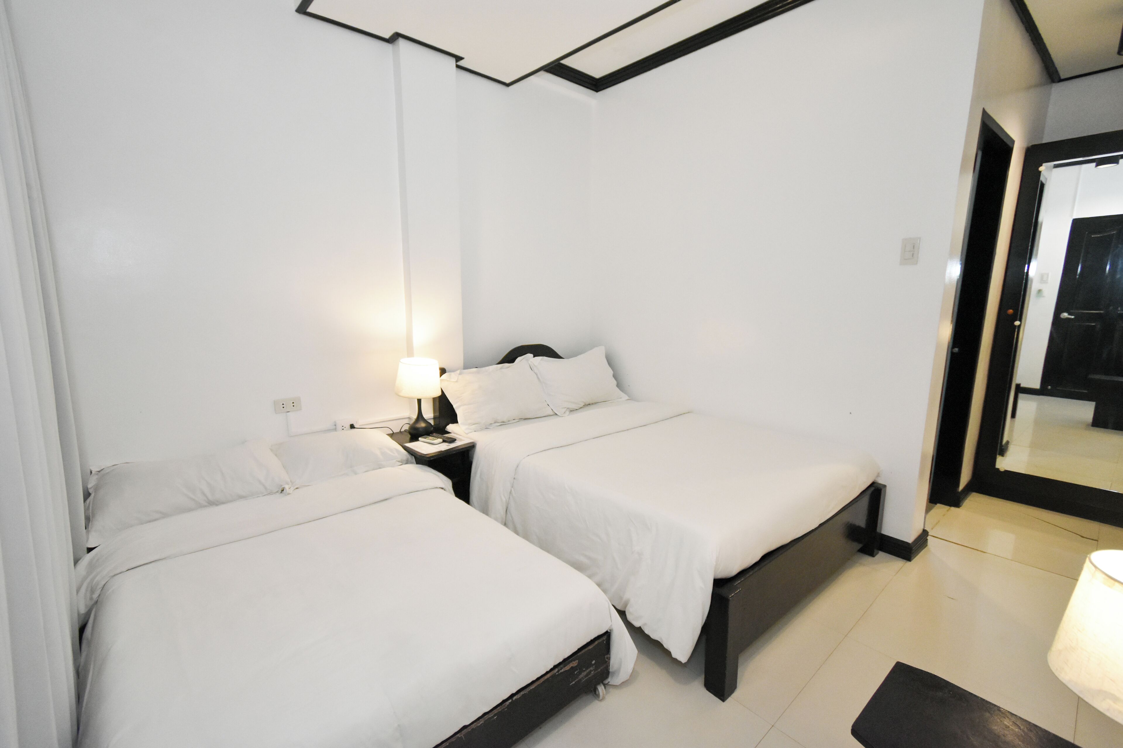 A hotel room with two beds, a nightstand with a lamp, and a large mirror.