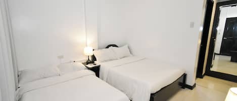 A hotel room with two beds, a nightstand with a lamp, and a large mirror.