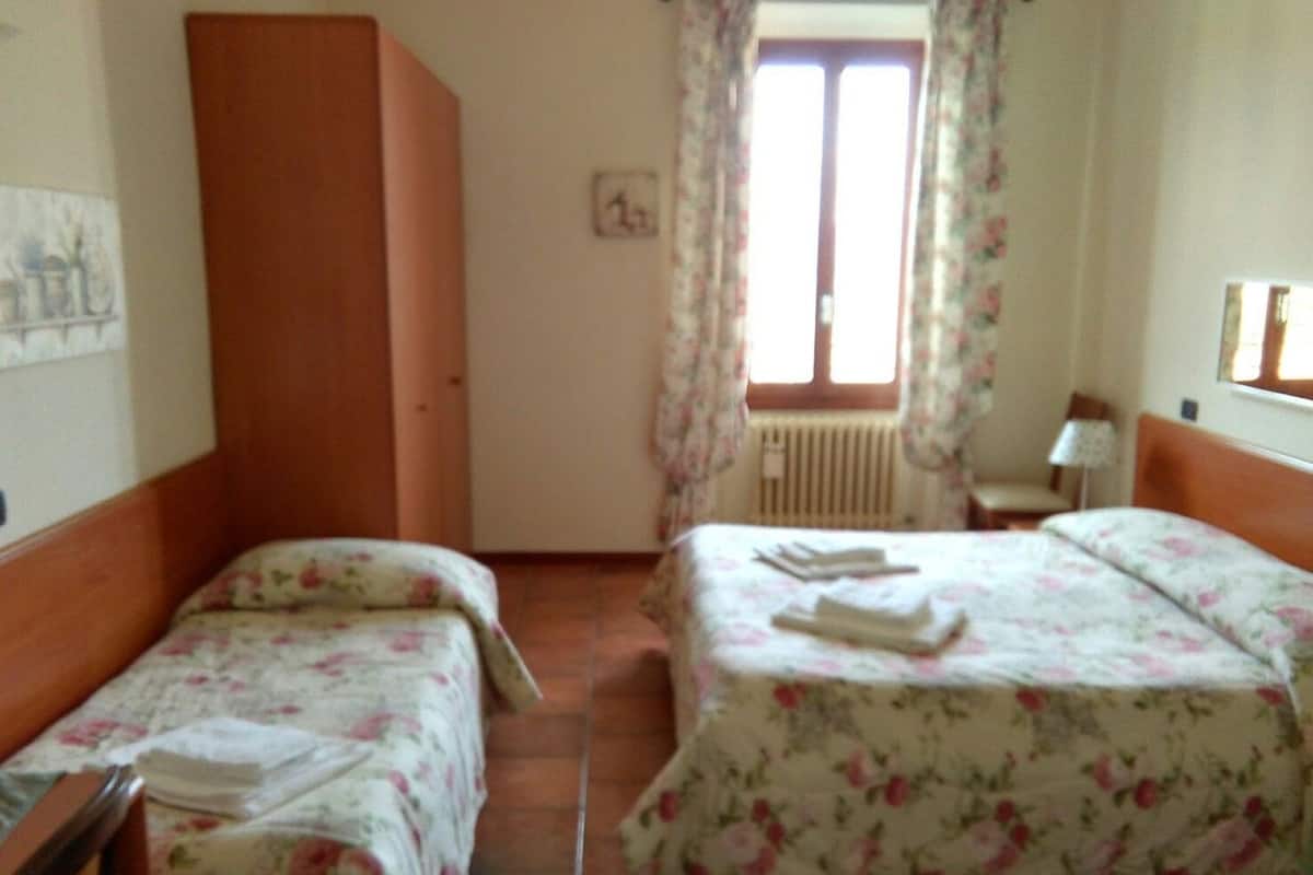 Una habitación con dos camas individuales, un armario de madera, un radiador y una ventana con cortinas florales.